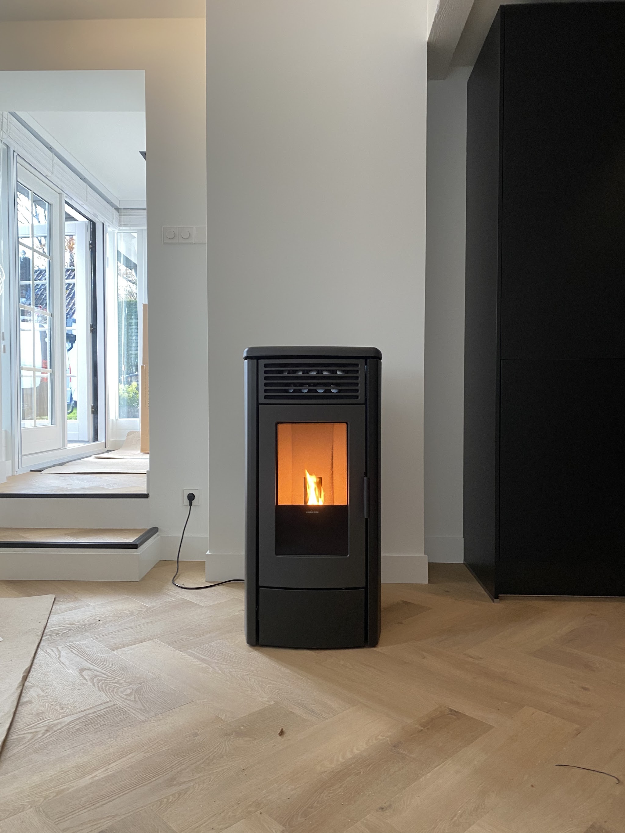 Een zwarte pelletkachel met een brandend vuur in een lichte kamer met een visgraatvloer.